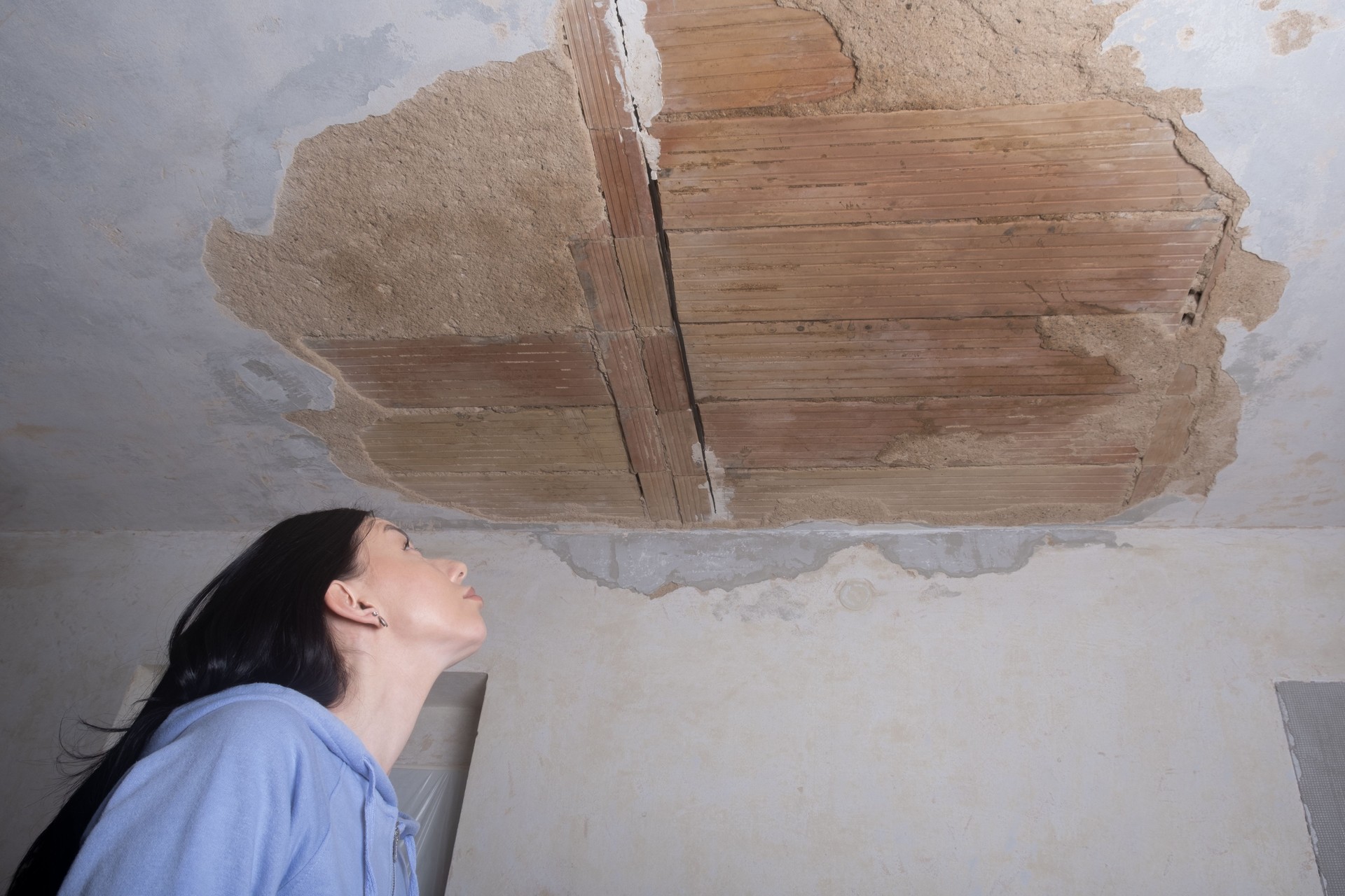 a young woman looking up at a ruined hole in the ceiling. The plaster fell off from moisture. Old apartment  restoration repair and fixing.